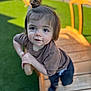 toddler, child, top_knot, wooden_railing, outdoor, green_turf, playground, curious, brown_shirt, blue_pants, daylight, fence, young_child, person, portrait, smile, baby, grass, wood, play_area