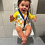 Sage is registered to the contest to win money with this photo: toddler, child, smiling, happy, yellow_clothing, headband, sitting, chair, indoor, strap, patterned_outfit, barefoot, waving, face, person, young_child, tile_wall, floor, cute, playful