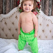 Sage joined the competition — help win amazing prizes! toddler, child, smiling, green_pants, bed, blanket, hair_tied, headboard, holiday_decor, red_berries, ribbon, indoor, portrait, bare_chest, happy, standing, cute, person, furry_clothing, light_skin