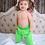 toddler, child, smiling, green_pants, bed, blanket, hair_tied, headboard, holiday_decor, red_berries, ribbon, indoor, portrait, bare_chest, happy, standing, cute, person, furry_clothing, light_skin