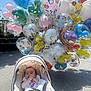 baby, car_seat, balloons, outdoor, sunny, cartoon_characters, colorful, child, infant, sidewalk, shade, happy, toy, mickey_mouse, disney, footwear, clothing, person, celebration, festive