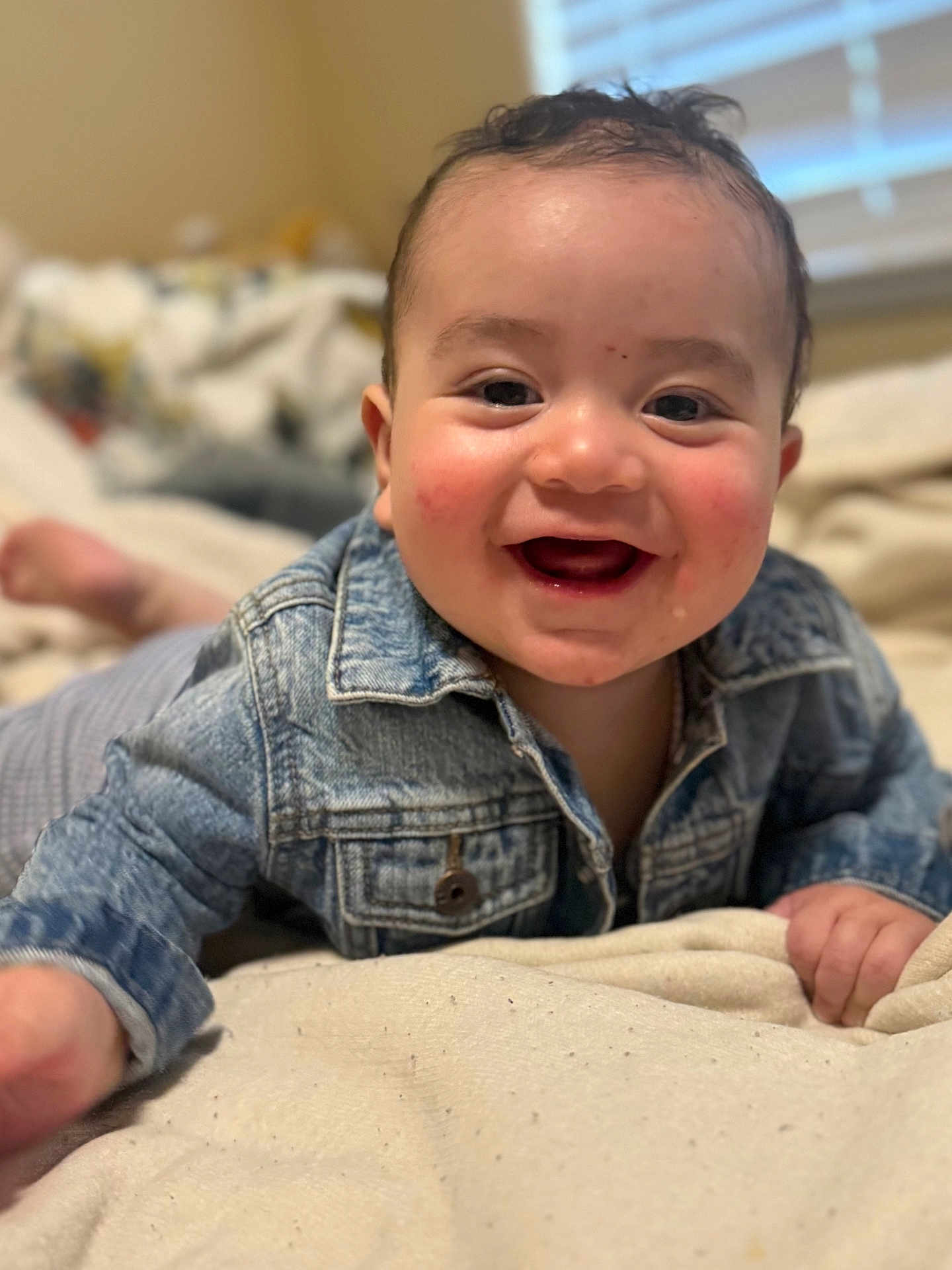 Valentino joined the competition — help win amazing prizes! baby, smiling, denim_jacket, infant, lying_down, bed, blanket, hand, face, happy, indoors, person, cute, child, skin, head, expression, reaching, window, casual_clothing