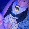 Dawson is registered to the contest to win money with this photo: baby, child, batman, pajamas, clothing, person, lap, blue_light, indoor, infant, cute, sitting, face, eyes, hand, adult, holding, foot, closeup, portrait