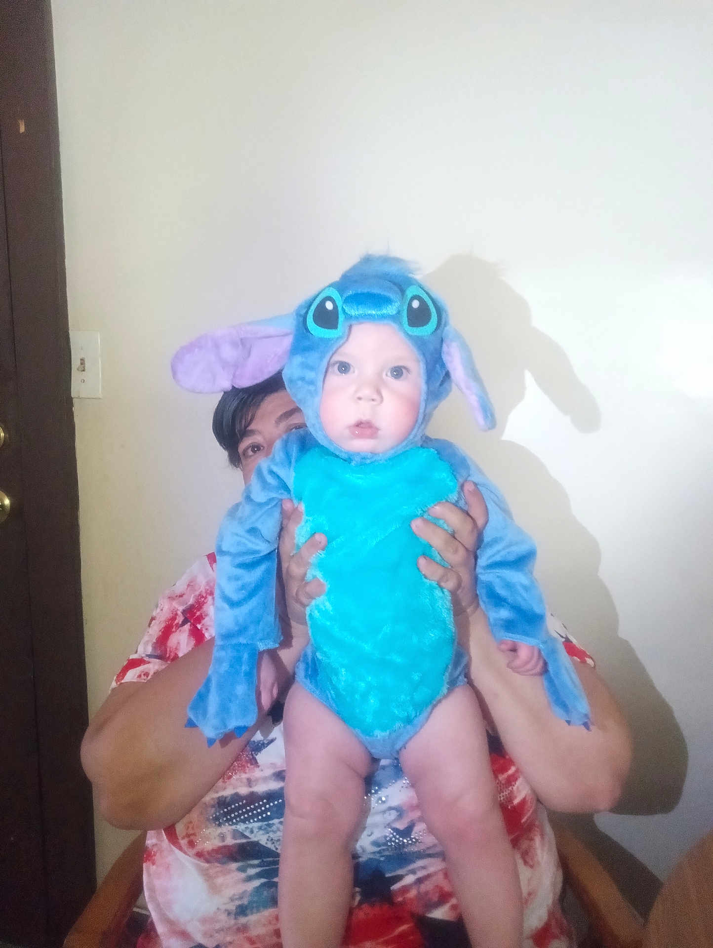 Calvin joined the competition — help win amazing prizes! baby, child, costume, blue, person, indoor, wall, door, hands, holding, seated, curious, face, eyes, clothing, adult, shadow, light, expression, furniture