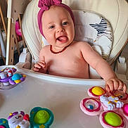 Louna a rejoint le concours — aidez-le/la à gagner de superbes lots ! amber_necklace, baby, butterfly_toy, child, colorful, cute, expression, furniture, happy, headband, high_chair, home, indoor, infant, person, playful, seat, smiling, tongue_out, toy