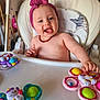 amber_necklace, baby, butterfly_toy, child, colorful, cute, expression, furniture, happy, headband, high_chair, home, indoor, infant, person, playful, seat, smiling, tongue_out, toy