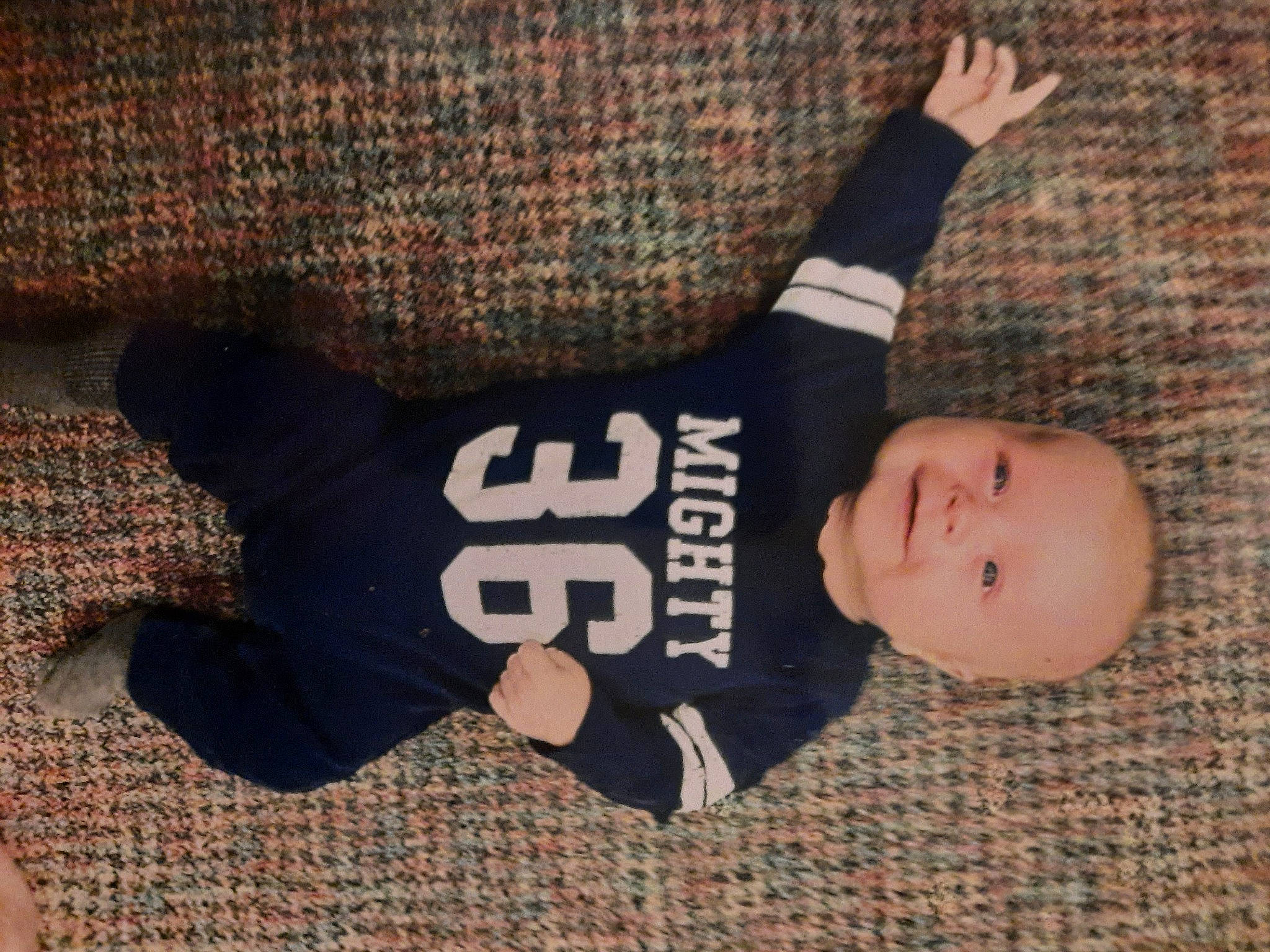 Evan is registered to the contest to win money with this photo: arm, baby, baby_toddler_clothing, comfort, facial_expression, finger, flooring, font, gesture, hand, happy, human_body, pattern, person, sleeve, smile, t_shirt, textile, thumb, toddler
