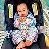baby, car_seat, toy, pajamas, child, outdoor, foot, face, seatbelt, infant, curious, sunlight, pavement, clothing, cute, hand, expression, sitting, childcare, safety