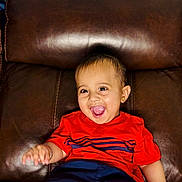 Vardaan joined the competition — help win amazing prizes! toddler, child, smiling, happy, laughing, red_shirt, navy_shorts, leather_couch, indoor, portrait, cute, baby, sitting, young_child, joy, expression, person, head, face, casual_clothing