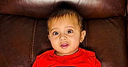 Vardaan joined the competition — help win amazing prizes! toddler, child, red_shirt, blue_shorts, brown_couch, indoor, sitting, curious, wide_eyes, leather, foot, hand, portrait, casual, young_child, home, furniture, cute, skin, person
