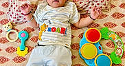 Vardaan is registered to the contest to win money with this photo: baby, child, infant, toys, bedspread, pattern, clothing, lion_king, smiling, cute, lying_down, colorful, playful, indoors, face, hands, feet, pillow, fabric, expression