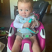 Jelisia joined the competition — help win amazing prizes! baby_seat, carpet, child, curly_hair, expression, furniture, green, holding, indoor, infant, kitchen, living_room, person, pink, seat_belt, toddler, toy, white, window, wooden_cabinet