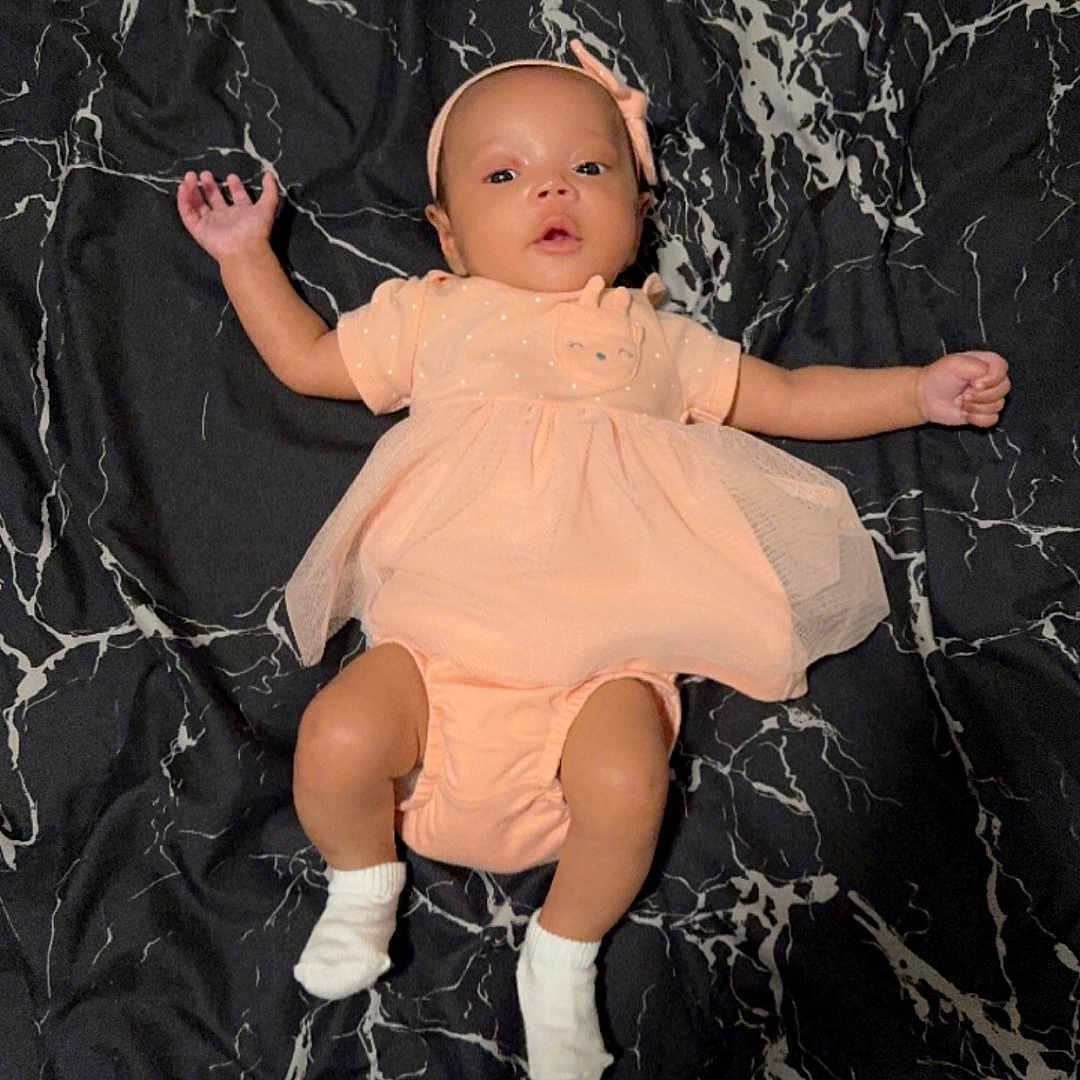 Yarelis joined the competition — help win amazing prizes! baby, bodypart, clothing, costume, diaper, dress, face, finger, footwear, formalwear, hand, head, hosiery, person, photography, portrait, shoe, sitting, sock, toy