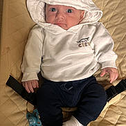 Ayden a rejoint le concours — aidez-le/la à gagner de superbes lots ! baby, hoodie, white_clothing, pacifier, infant, cute, child, sitting, blue_pants, white_socks, quilted_surface, indoor, looking_up, small_hands, face, expression, casual_clothing, soft_lighting, young_child, clothing