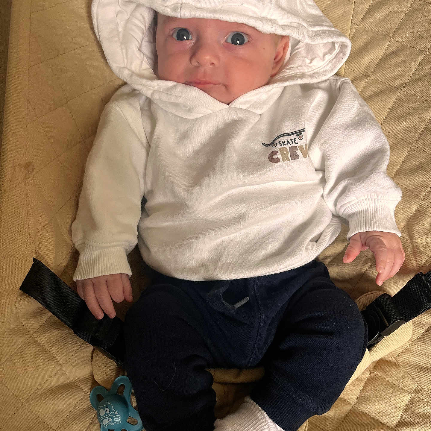 Ayden a rejoint le concours — aidez-le/la à gagner de superbes lots ! baby, blue_pants, casual_clothing, child, clothing, cute, expression, face, hoodie, indoor, infant, looking_up, pacifier, quilted_surface, sitting, small_hands, soft_lighting, white_clothing, white_socks, young_child