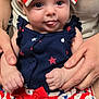 baby, child, infant, blue_eyes, bow, red_white_blue, stars, stripes, clothing, cute, tongue_out, hands, person, holding, pattern, skirt, sitting, portrait, smiling, closeup