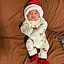 baby, infant, christmas_hat, pajamas, mittens, booties, blanket, brown, holiday, festive, cute, lying_down, indoors, person, face, expression, sleepwear, soft, cozy, child