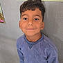 Younis participe au concours pour gagner de l'argent avec cette photo : child, boy, smiling, blue_clothing, portrait, casual_wear, standing, indoor, school, drawing, wall, happy, face, short_hair, young, person, looking_up, sleeves, pants, floor