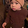 toddler, child, indoor, brown_sweater, beanie, curious, standing, furniture, patterned, carpet, leopard_print, pants, socks, young_child, warm_clothing, face, expression, home, floor, portrait