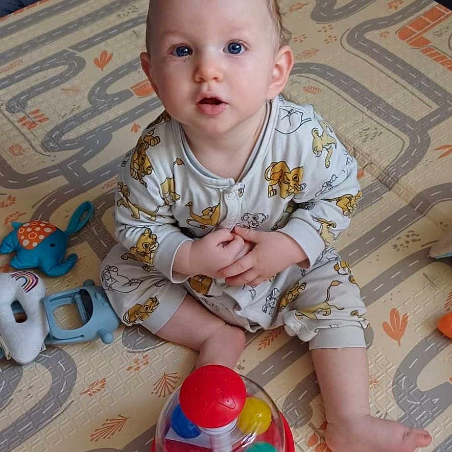 Dwayne Flaux-Vaz a rejoint le concours — aidez-le/la à gagner de superbes lots ! baby, barefoot, blue_eyes, child, curly_hair, cute, floor_mat, hands_clasped, indoor, infant, light_skin, looking_up, octopus_toy, onesie, playmat, plush_toy, road_pattern, sitting, spinning_ball_toy, toy