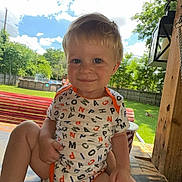 Dakota Jr is registered to the contest to win money with this photo: toddler, child, smiling, onesie, alphabet_pattern, bench, wood, outdoor, backyard, grass, trees, fence, pool, sky, clouds, sunny, face, person, daylight, shade