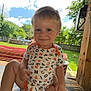 toddler, child, smiling, onesie, alphabet_pattern, bench, wood, outdoor, backyard, grass, trees, fence, pool, sky, clouds, sunny, face, person, daylight, shade