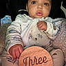 Makari is registered to the contest to win money with this photo: baby, infant, three_months, wooden_sign, blanket, sleeper, hand, face, portrait, cute, child, indoors, soft_lighting, newborn, young_child, sitting, cozy, expression, clothing, person