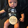 baby, infant, child, onesie, black_clothing, wooden_sign, text, three_months, sitting, portrait, indoor, cute, face, hands, legs, skin, expression, dark_background, photography, person