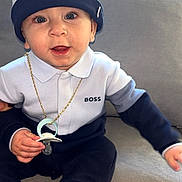 Liam participe au concours pour gagner de l'argent avec cette photo : baby, child, pacifier, hat, clothing, blue, white, couch, indoor, person, portrait, face, sitting, cute, smile, gold_chain, fashion, infant, young_child, accessory