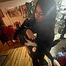 Francis is registered to the contest to win money with this photo: indoor, person, cat, black_cat, white_paws, holding, wood_floor, kitchen, dining_chair, refrigerator, magnet, paper, plant, lamp, painting, curly_hair, casual_clothing, soft_light, blur, home