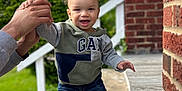 Kyrie joined the competition — help win amazing prizes! child, toddler, smiling, hoodie, jeans, white_sneakers, hand_holding, porch, brick_wall, greenery, outdoor, daylight, curly_hair, person, happy, walking, support, baby, casual_clothing, blue_sky