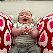 Onyx joined the competition — help win amazing prizes! baby, infant, smiling, laughing, face, hands, onesie, striped_onesie, gray_pants, red_pillows, heart_pattern, cushion, plush_blanket, wall_art, indoor, portrait, seated, cozy, happy, chubby_cheeks