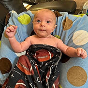 Caeson joined the competition — help win amazing prizes! baby, blanket, cushion, polka_dot, football, infant, person, indoor, furniture, leather_chair, curious, eyes, hand, face, head, pattern, soft, comfort, wrapped, lying