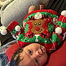 baby, child, infant, face, christmas_sweater, reindeer, red, green, cushion, blanket, home, indoors, cozy, cute, smiling, person, clothing, holiday, festive, lying_down