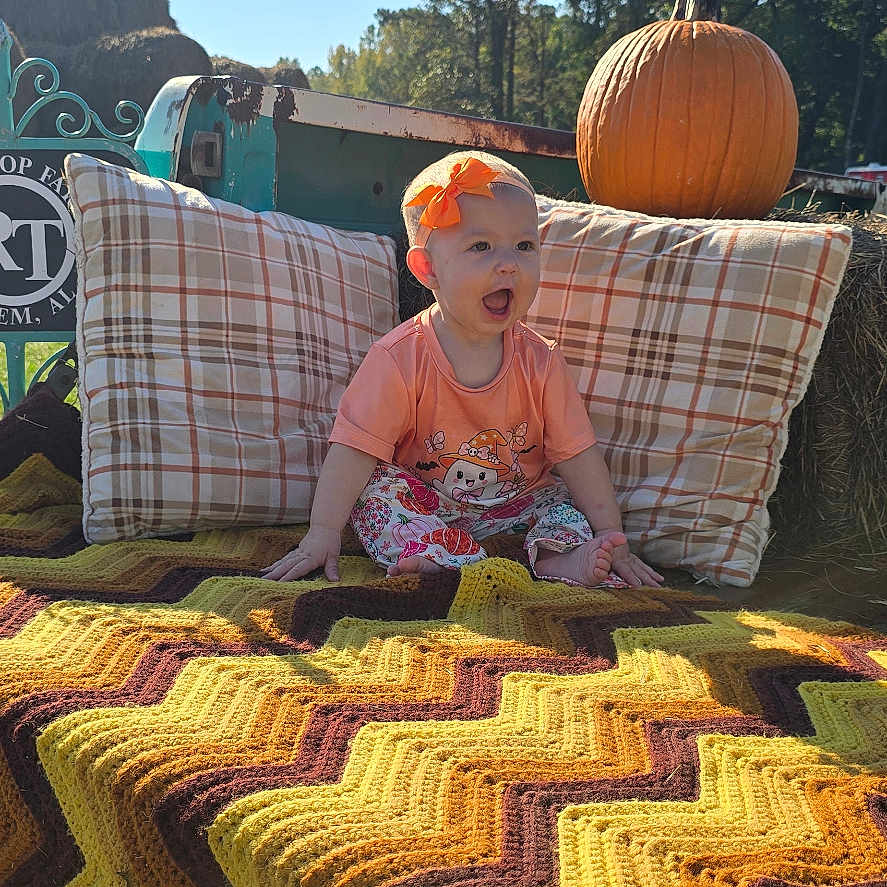 Nova Leigh is registered to the contest to win money with this photo: child, toddler, outdoor, autumn, pumpkin, blanket, hay_bale, orange_bow, smiling, open_mouth, sitting, portrait, sunlight, blue_sky, trees, grass, farm, fall_decor, colorful, cozy