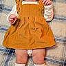 Nova Leigh is registered to the contest to win money with this photo: baby, child, infant, smiling, happy, lying_down, portrait, plaid_blanket, mustard_dress, pinafore, bow_headband, socks, shoes, fashion, indoor, close_up, full_body, cozy, playful, photography