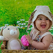 Hallie is registered to the contest to win money with this photo: baby, child, smiling, hat, bonnet, toy, stuffed_animal, bunny, basket, flower, greenery, daisy, cute, happy, infant, portrait, playful, indoors, colorful, young