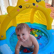 Donovin joined the competition — help win amazing prizes! toddler, child, inflatable_pool, water, yellow_canopy, toys, outdoor, smiling, playful, summer, sunny, baby, blue_pool, plastic, skin, happy, cute, young_child, person, daytime