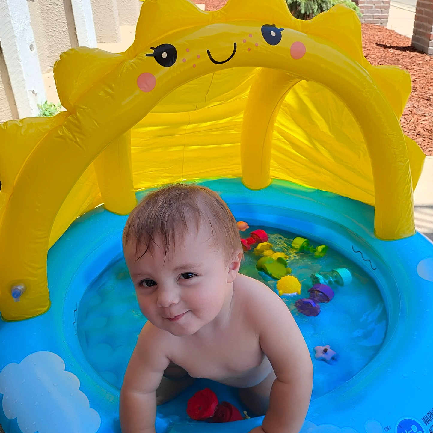Donovin joined the competition — help win amazing prizes! toddler, child, inflatable_pool, water, yellow_canopy, toys, outdoor, smiling, playful, summer, sunny, baby, blue_pool, plastic, skin, happy, cute, young_child, person, daytime