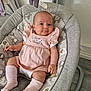 baby, infant, pink_dress, baby_rocker, elephant_print, sock, toy, purple_toy, floor, wooden_floor, cushion, fabric, child, indoor, smile, person, cute, comfort, seat, resting