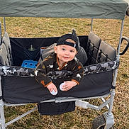 Colter is registered to the contest to win money with this photo: toddler, child, wagon, cap, outdoor, grass, lake, trees, canopy, toy, playful, curious, camo_pattern, wheel, field, nature, daylight, smiling, person, recreation