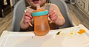Colter is registered to the contest to win money with this photo: toddler, child, high_chair, sippy_cup, kitchen, floor, hand, food, messy, baby, smiling, plastic, furniture, cabinet, appliance, person, foot, table, drink, indoor