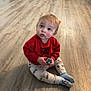 toddler, child, sitting, red_sweatshirt, toy, wooden_floor, indoor, kitchen, refrigerator, curious, pants, socks, flooring, home, childhood, person, young_child, casual_clothing, looking_up, cute