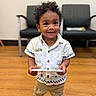 Adonis joined the competition — help win amazing prizes! toddler, child, curly_hair, white_shirt, khaki_pants, tablet, twenty_dollar_bill, indoor, wooden_floor, chairs, smiling, standing, casual_clothing, cute, young_child, person, technology, happy, portrait, holding