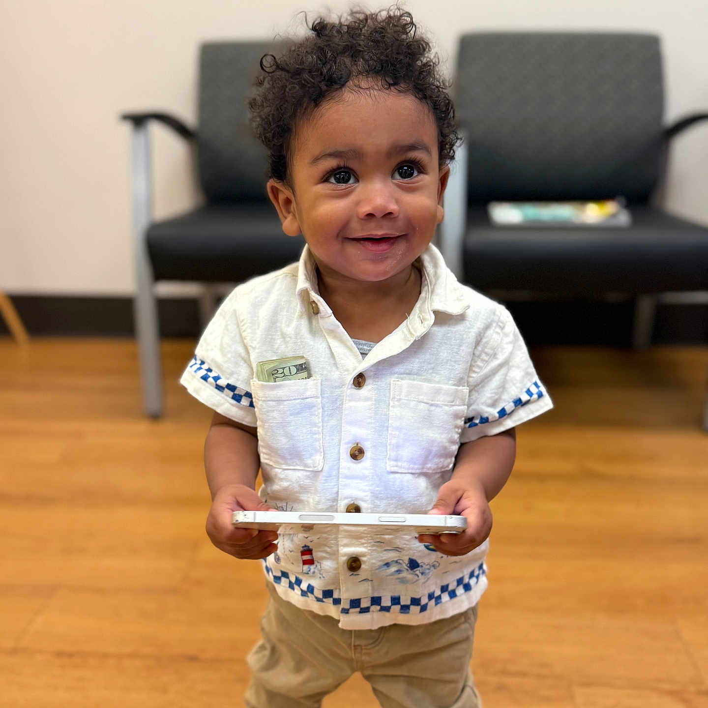 Adonis joined the competition — help win amazing prizes! toddler, child, curly_hair, white_shirt, khaki_pants, tablet, twenty_dollar_bill, indoor, wooden_floor, chairs, smiling, standing, casual_clothing, cute, young_child, person, technology, happy, portrait, holding