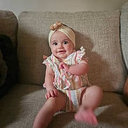 Hazel joined the competition — help win amazing prizes! baby, child, infant, headband, striped_clothing, couch, beige, smile, happy, sitting, foot, hand, indoors, cute, young, portrait, person, cozy, home, playful
