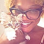 person, cat, kitten, glasses, smile, curly_hair, blonde_hair, face, hand, fur, indoor, closeup, portrait, cute, pet, holding, warm_lighting, cozy, happy, feline