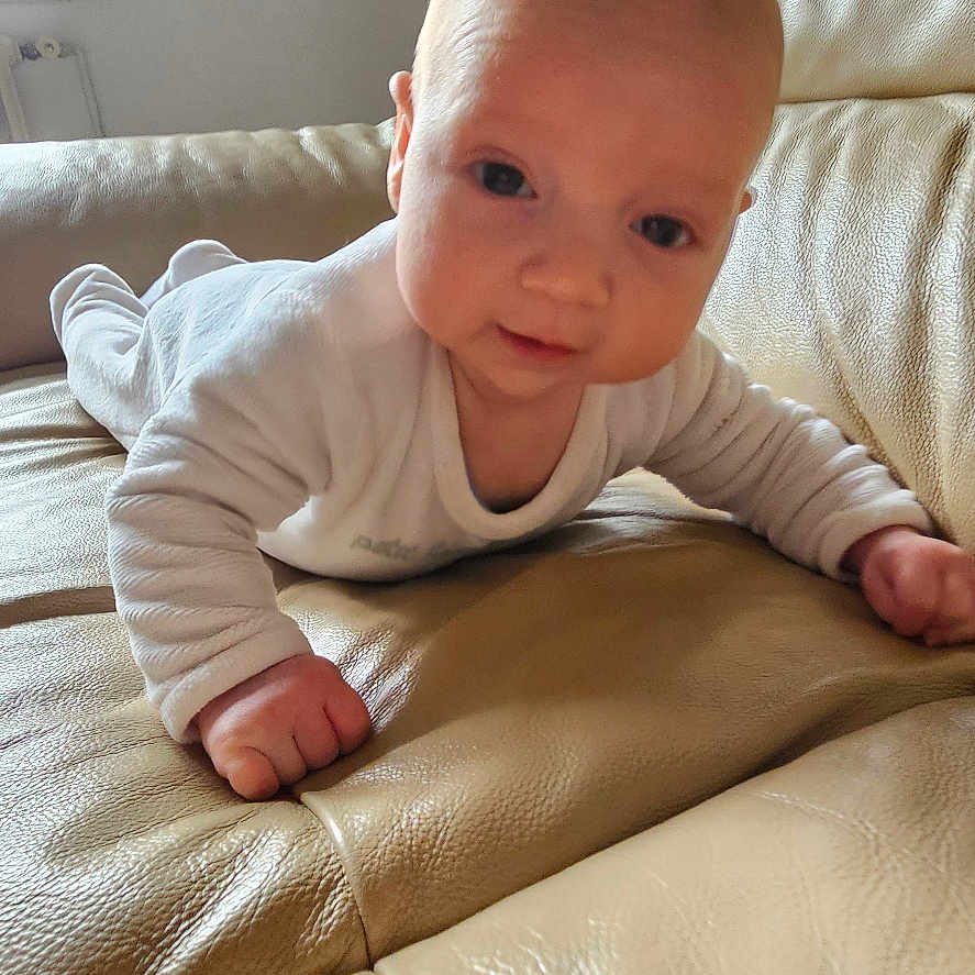 Malo is registered to the contest to win money with this photo: baby, infant, couch, leather, indoor, person, child, face, smiling, curious, white_clothing, home, window, skin, young, toddler, furniture, light, portrait, hands