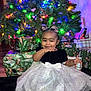 Laysia is registered to the contest to win money with this photo: bow, celebration, child, christmas_lights, christmas_tree, cute, dress, family, festive, gift_wrap, hair_bow, happy, holiday, holiday_decor, indoor, presents, sitting, smile, sparkle, toddler
