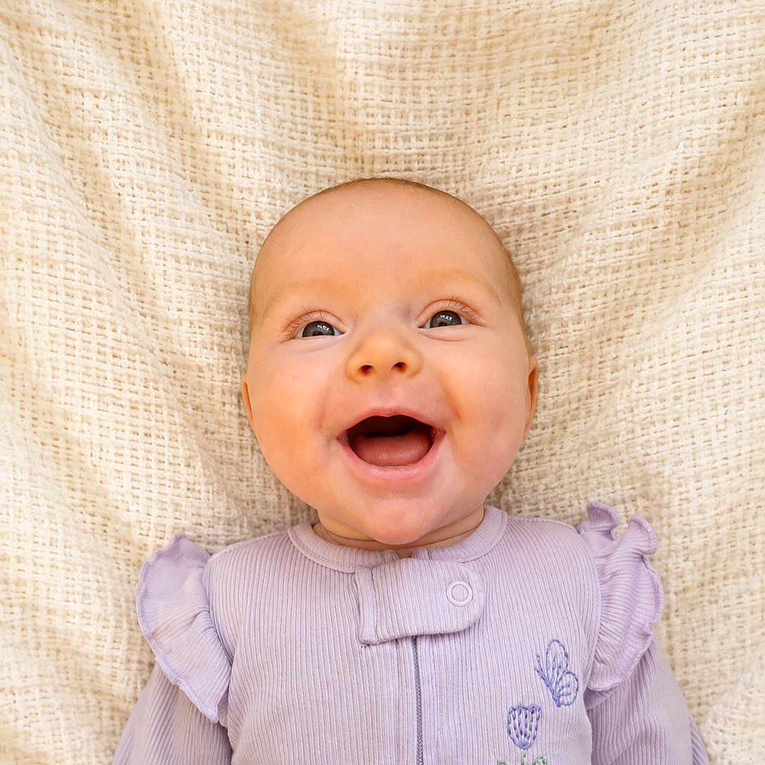 Josette is registered to the contest to win money with this photo: baby, smiling, infant, face, portrait, clothing, purple, embroidery, butterfly, flower, blanket, texture, happy, cute, child, young, lying_down, closeup, skin, cute_baby
